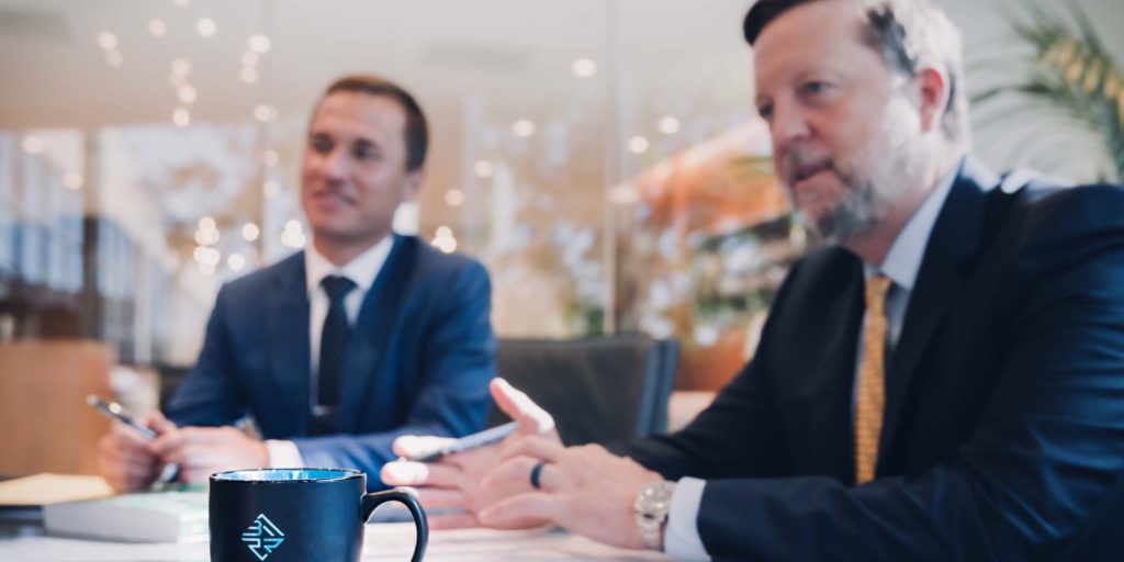 Two of our medical malpractice lawyers in Jackson County sit in our office, discussing a potential case with a victim of potential negligence. A coffee mug bearing the BFRR logo sits closest to the viewer, with the lawyers in the background. 