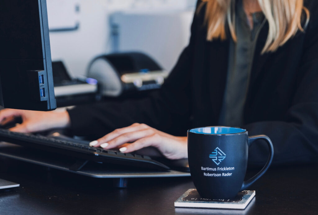 A close up of a woman at a desk, typing on her keyboard and a BFRR coffee mug to her left. She is a Truck Wreck Attorney in Johnson County.
